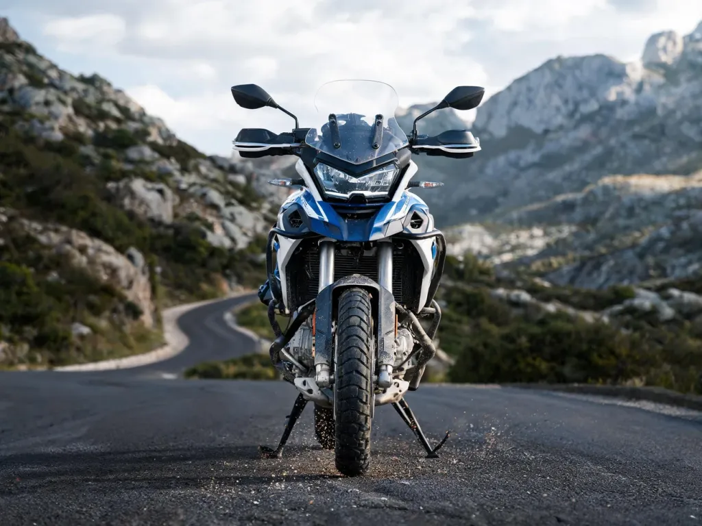 CFMoto 450MT z przodu na górskiej drodze, podkreślone zawieszenie, koło i silnik, w tle kręta szosa i góry