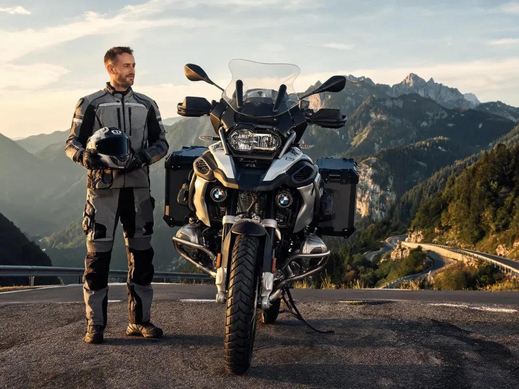BMW R 1250 GS Adventure zaparkowany na górskiej przełęczy, z motocyklistą obok i krętą drogą w tle